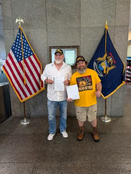 Anthony Hudson and Jason Dye holding their candidate filing paperwork in front of the United States and Michigan flags