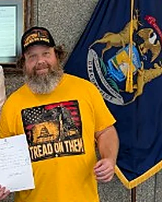 Jason Dye in his black campaign cap and gold Tread on Them shirt, holding his candidate filing paperwork